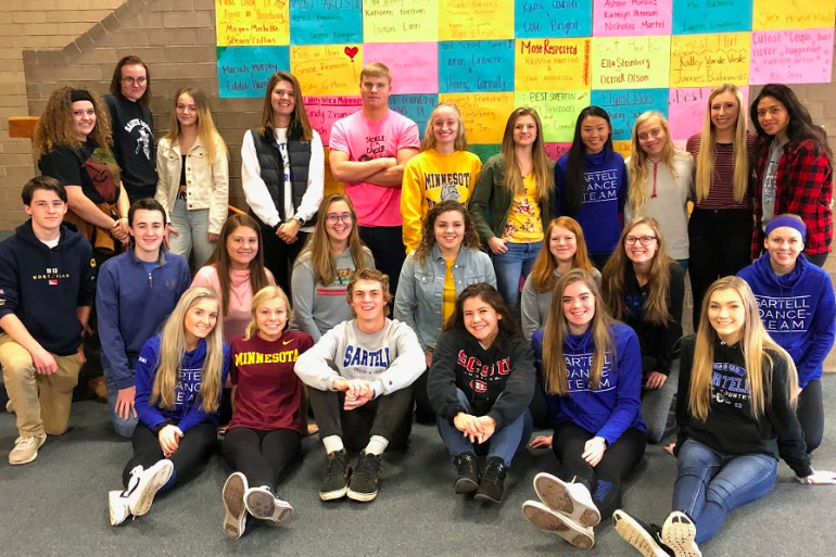 Quarter 1 yearbook staff posing in front of the wall advertisement. 